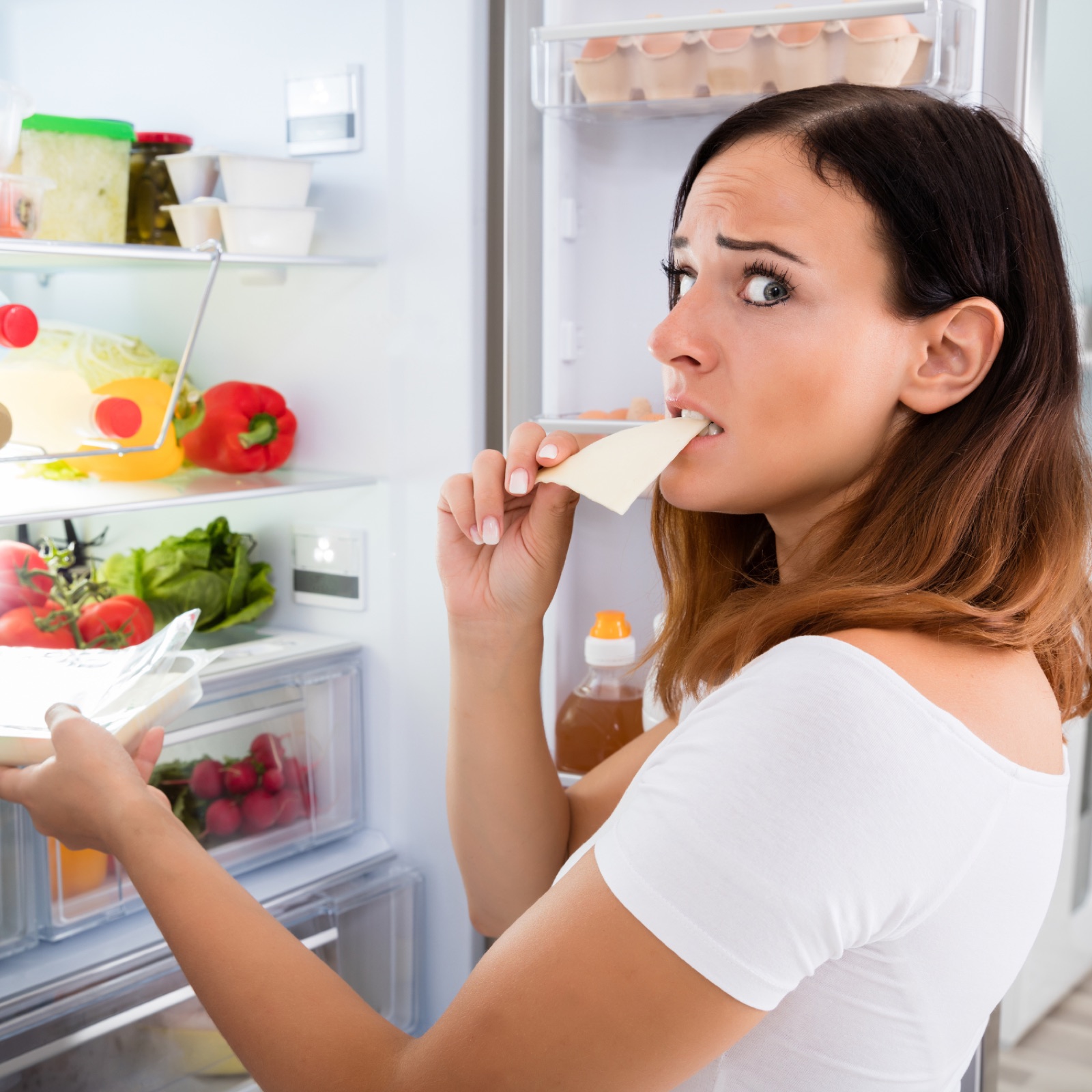 A woman standing at an open fridge deciding what to eat, support for a healthy relationship with food in Brisbane